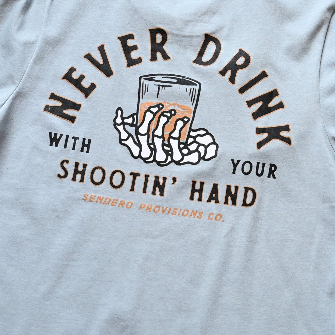 View of Sendero Big Sky Blue graphic tee with “Never drink with your shooting hand” print