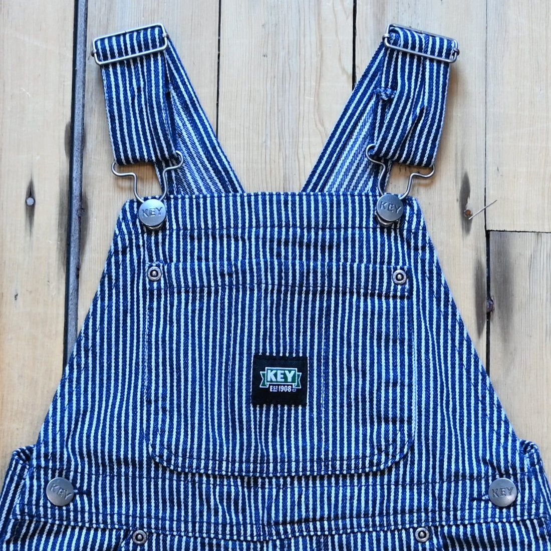 View of Detail of kids KEY bib overall in blue denim and stripped with pockets.