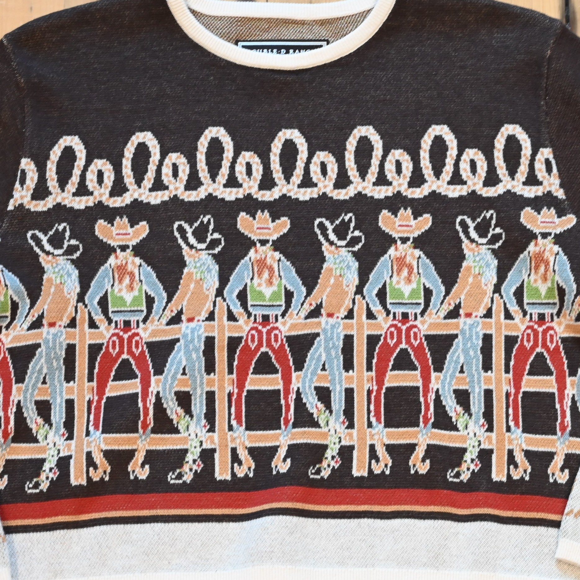 View of Long Tall Texan cropped sweater in bronco brown with embroidered cowboy characters, contrasting cuffs, and rope detail