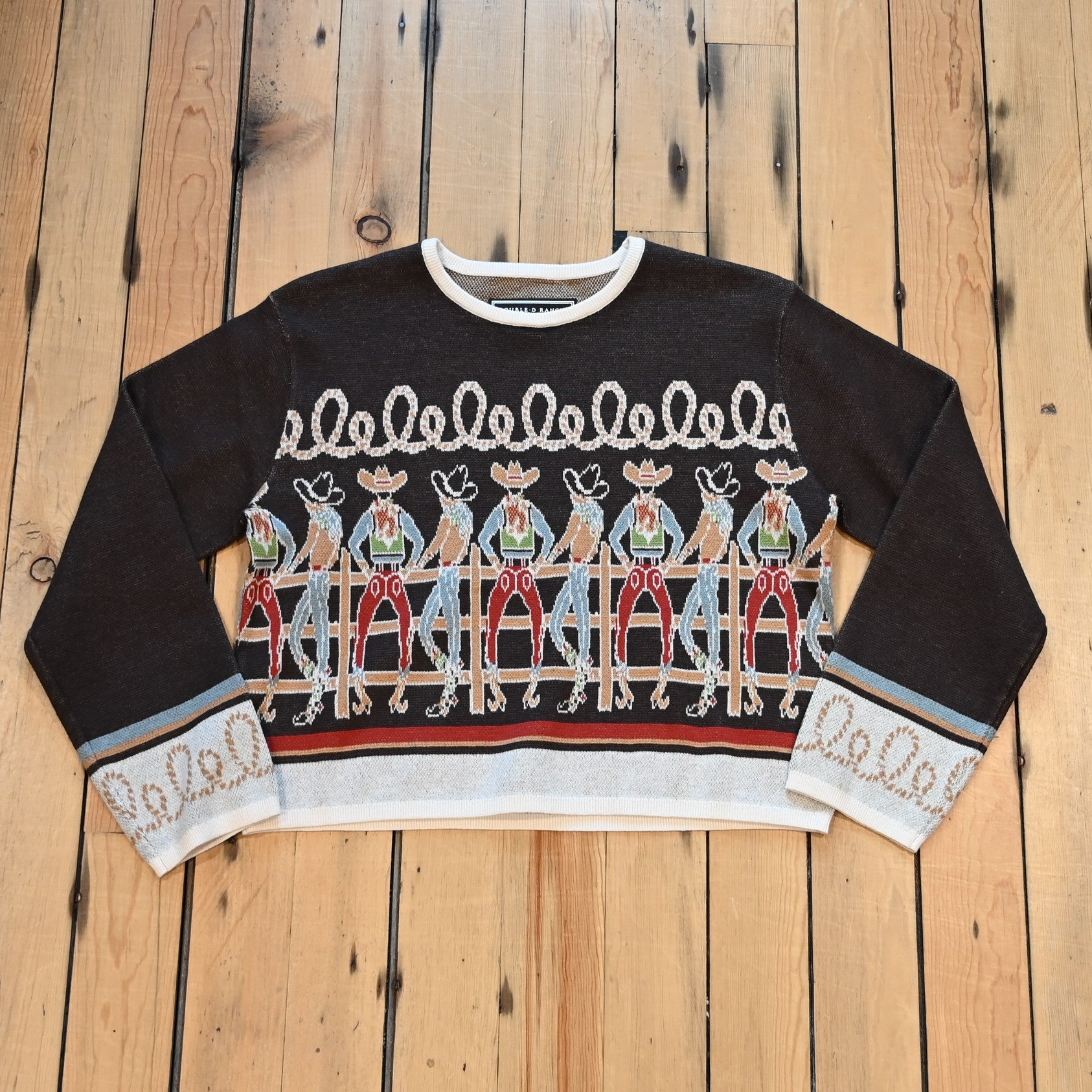 View of Long Tall Texan cropped sweater in bronco brown with embroidered cowboy characters, contrasting cuffs, and rope detail