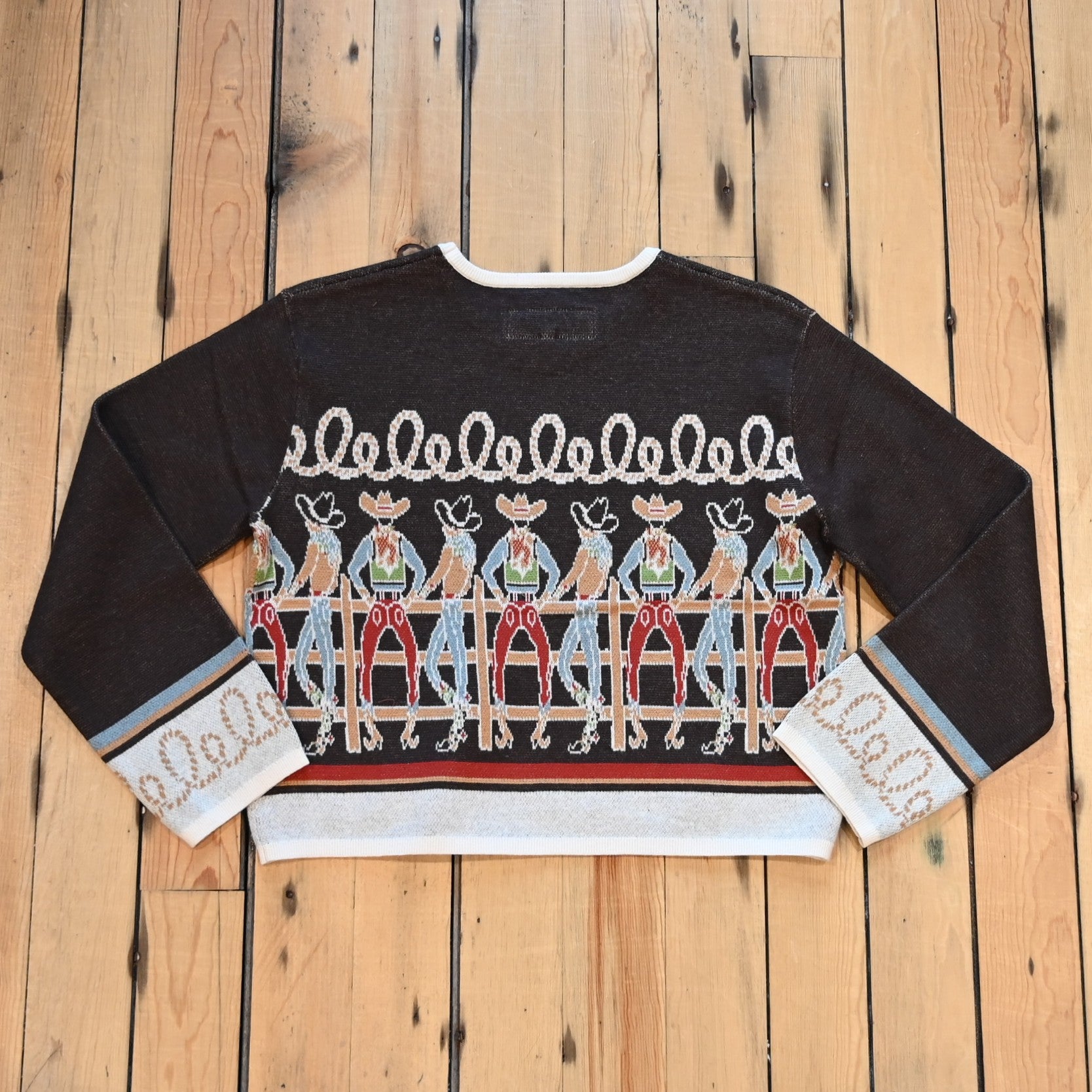 View of Long Tall Texan cropped sweater in bronco brown with embroidered cowboy characters, contrasting cuffs, and rope detail