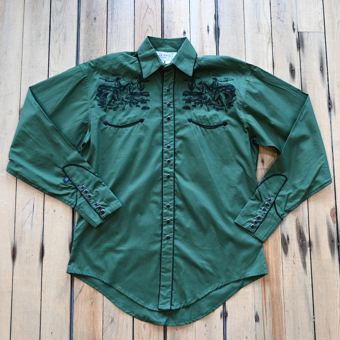 View of Green Western shirt with embroidered “man and rider” motif across yokes and cuffs